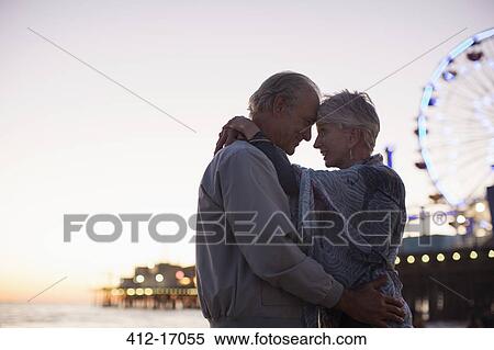 Stock Photography - Senior couple hugging on beach at sunset. Fotosearch