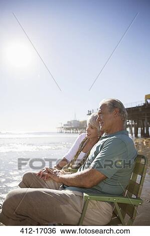 Stock Photograph - Senior couple relaxing in lawn chairs on beach. Fotosearch