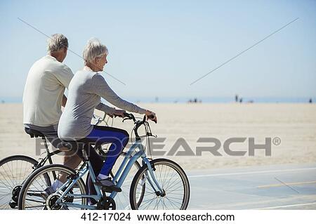 Picture - Senior couple riding bicycles on beach. Fotosearch