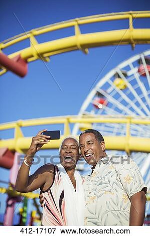 Stock Photo - Senior couple taking selfie at amusement park. Fotosearch
