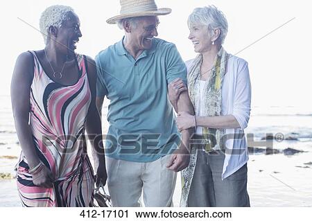 Stock Image - Senior friends walking on beach. Fotosearch
