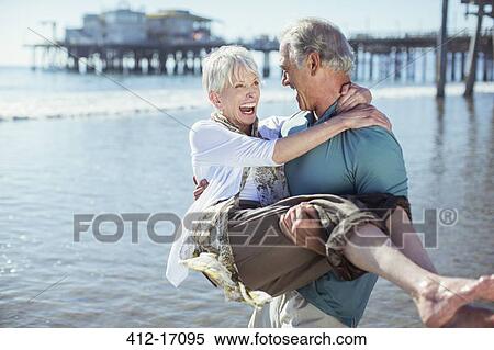 Senior man carrying wife on sunny beach View Large Photo Image Stock Photography - Senior man carrying wife on sunny beach. Fotosearch