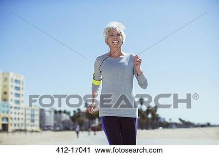 Stock Image - Senior woman power walking on beach. Fotosearch