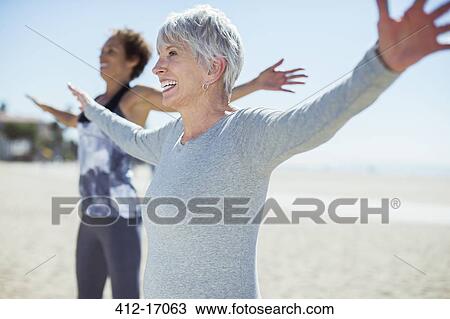 Stock Image - Senior women stretching arms on beach. Fotosearch