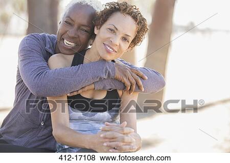 Stock Photo - Smiling women hugging outdoors. Fotosearch