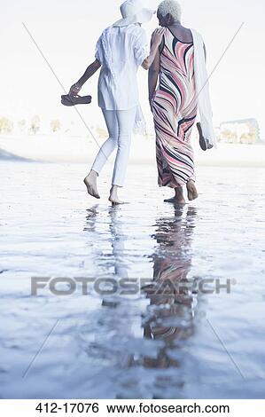 Stock Photograph - Women walking barefoot on beach. Fotosearch