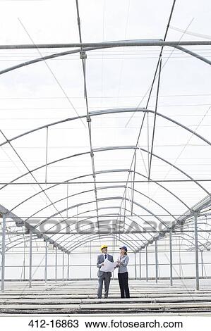 Stock Image - Architect and businesswoman reviewing blueprint in empty greenhouse. Fotosearch