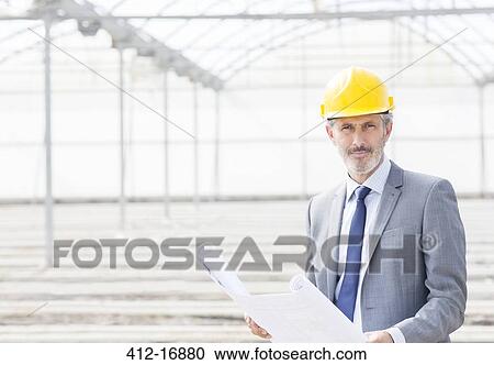 Stock Image - Portrait of confident architect with blueprint in greenhouse. Fotosearch
