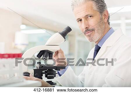 Stock Image - Portrait of confident scientist using microscope in laboratory. Fotosearch