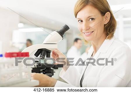 Stock Photography - Portrait of confident scientist using microscope in laboratory. Fotosearch