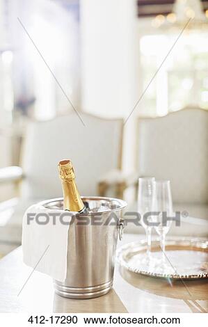 Stock Image - Champagne in silver bucket next to champagne flutes. Fotosearch
