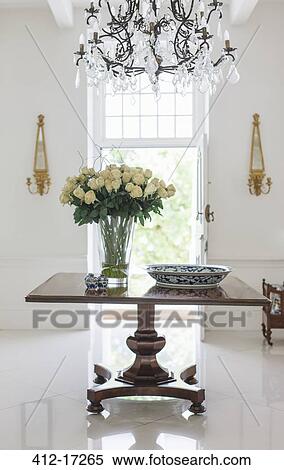 Stock Photography - Chandelier over bouquet on table in luxury foyer. Fotosearch