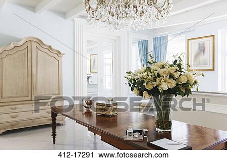 Stock Image - Chandelier over rose bouquet on table in luxury foyer. Fotosearch