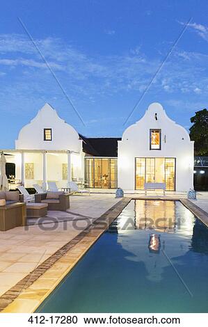 Stock Image - Luxury house and lap pool illuminated at night. Fotosearch
