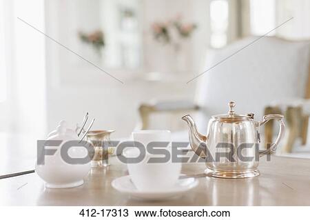 Stock Image - Teacups and silver teapot on table. Fotosearch
