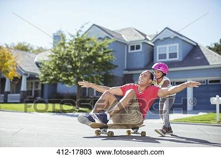Stock Image - Daughter pushing father on skateboard. Fotosearch