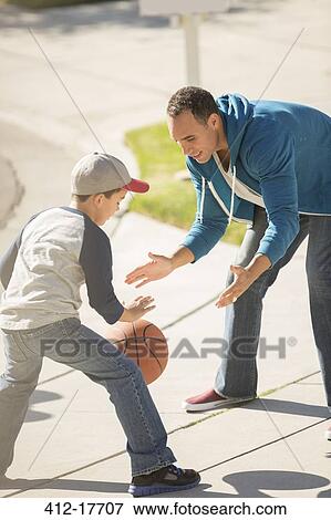Stock Photo - Father and son playing basketball in sunny driveway. Fotosearch