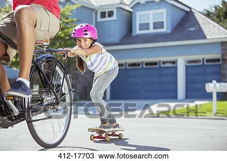 Father on bicycle pulling daughter on skateboard View Large Photo Image Stock Image - Father on bicycle pulling daughter on skateboard. Fotosearch