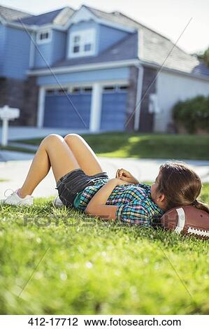 Girl laying on football in grass outside house View Large Photo Image Stock Image - Girl laying on football in grass outside house. Fotosearch