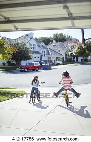 Girls riding bicycles in sunny driveway View Large Photo Image Stock Photograph - Girls riding bicycles in sunny driveway. Fotosearch