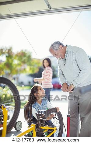 Stock Image - Grandfather and granddaughter inflating bicycle tire. Fotosearch