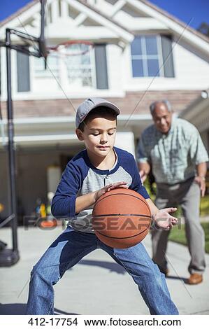 Picture - Grandfather and grandson playing basketball in driveway. Fotosearch