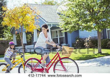 Picture - Mother and daughter riding bikes in street. Fotosearch