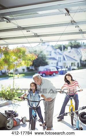 Picture - Multi-generation family riding bicycles in driveway. Fotosearch