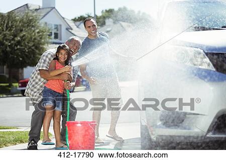 Stock Image - Multi-generation family washing car in driveway. Fotosearch