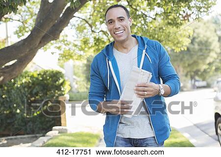 Stock Image - Portrait of smiling man with newspaper outdoors. Fotosearch