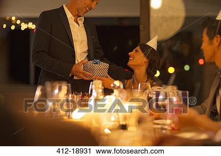 Stock Image - Man giving wife gift at birthday party. Fotosearch