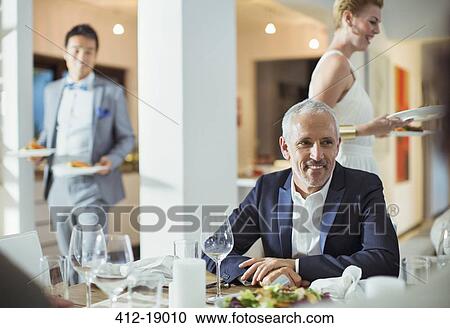 Stock Image - Man sitting at table at dinner party. Fotosearch