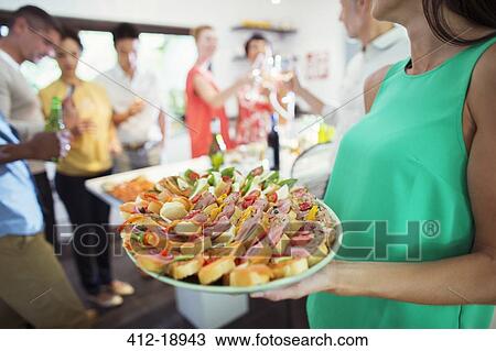 Stock Image - Woman serving tray of food at party. Fotosearch