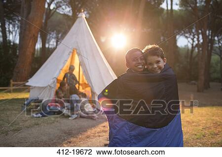 Stock Image - Boys wrapped in blanket at campsite. Fotosearch