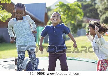 Stock Photo - Children jumping on trampoline outdoors. Fotosearch