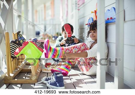 Stock Image - Children pulling on rainboots on porch. Fotosearch