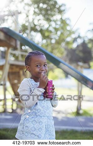 Stock Image - Girl drinking juice box at playground. Fotosearch