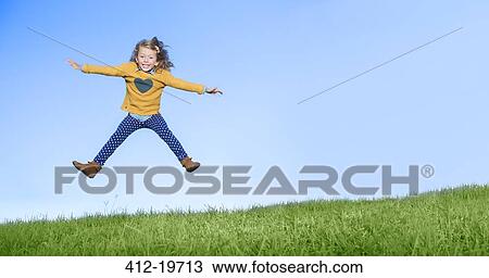 Stock Image - Girl jumping for joy on grassy hill. Fotosearch