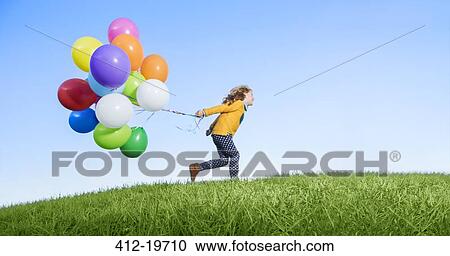 Stock Image - Girl playing with balloons on grassy hill. Fotosearch