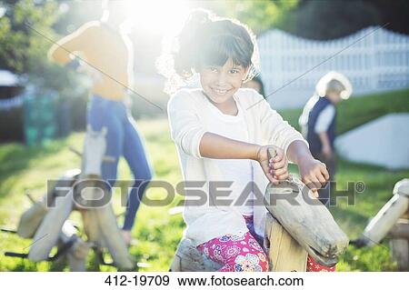 Girl smiling on rocking horse in playground View Large Photo Image Stock Photo - Girl smiling on rocking horse in playground. Fotosearch