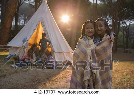 Stock Photo - Girls wrapped in blanket at campsite. Fotosearch