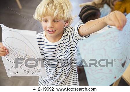 Stock Image - Student showing off drawings in classroom. Fotosearch