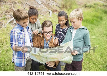 Stock Image - Students and teacher reading map outdoors. Fotosearch