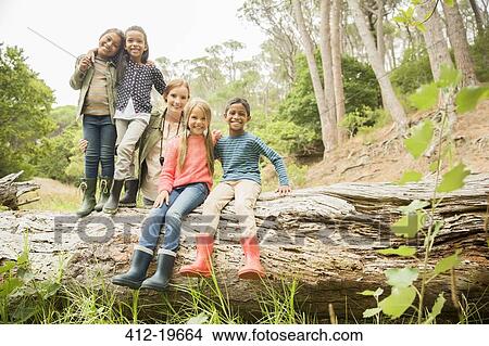 Picture - Students and teacher sitting on log in forest. Fotosearch