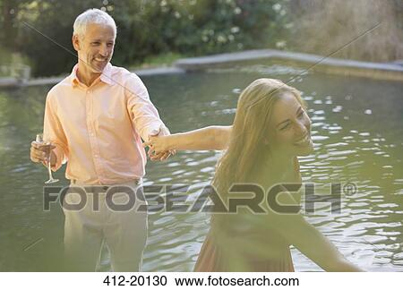 Stock Image - Couple holding hands by pool outdoors. Fotosearch