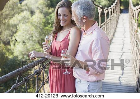 Stock Photo - Couple toasting each other on wooden rope bridge. Fotosearch
