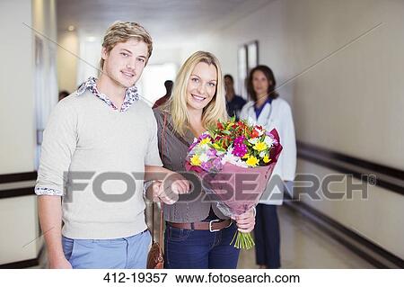Couple carrying bouquet of flowers in hospital View Large Photo Image Stock Photo - Couple carrying bouquet of flowers in hospital. Fotosearch