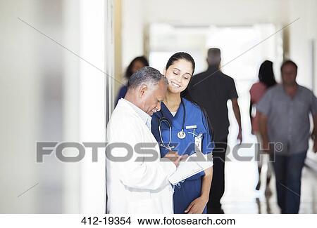 Picture - Doctor and nurse reading medical chart in hospital hallway. Fotosearch