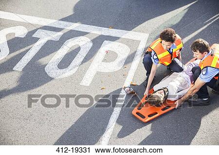 Stock Image - Paramedics examining injured girl on street. Fotosearch