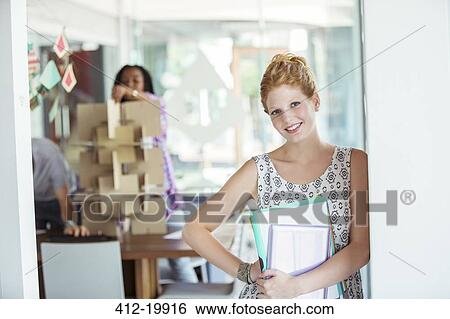 Stock Photograph - Businesswoman carrying binders in office. Fotosearch